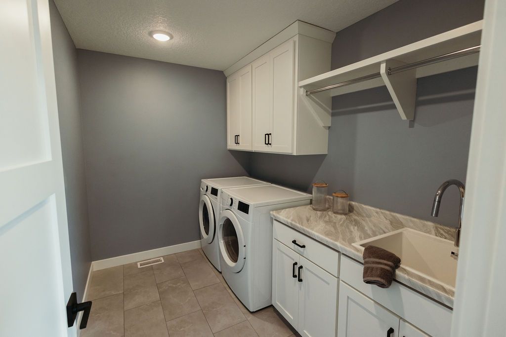 Laundry room with white cabinets, gray walls, washer/dryer, and a countertop with a sink.