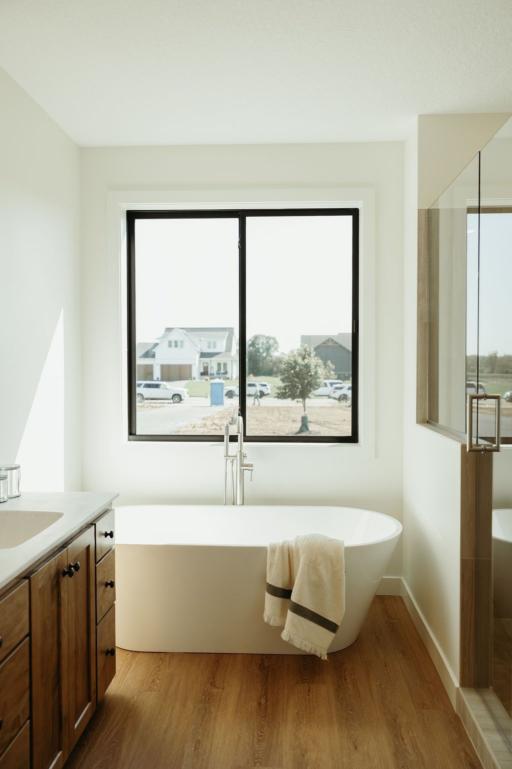 Bathroom with a freestanding bathtub in front of a window, wooden vanity, and glass shower.