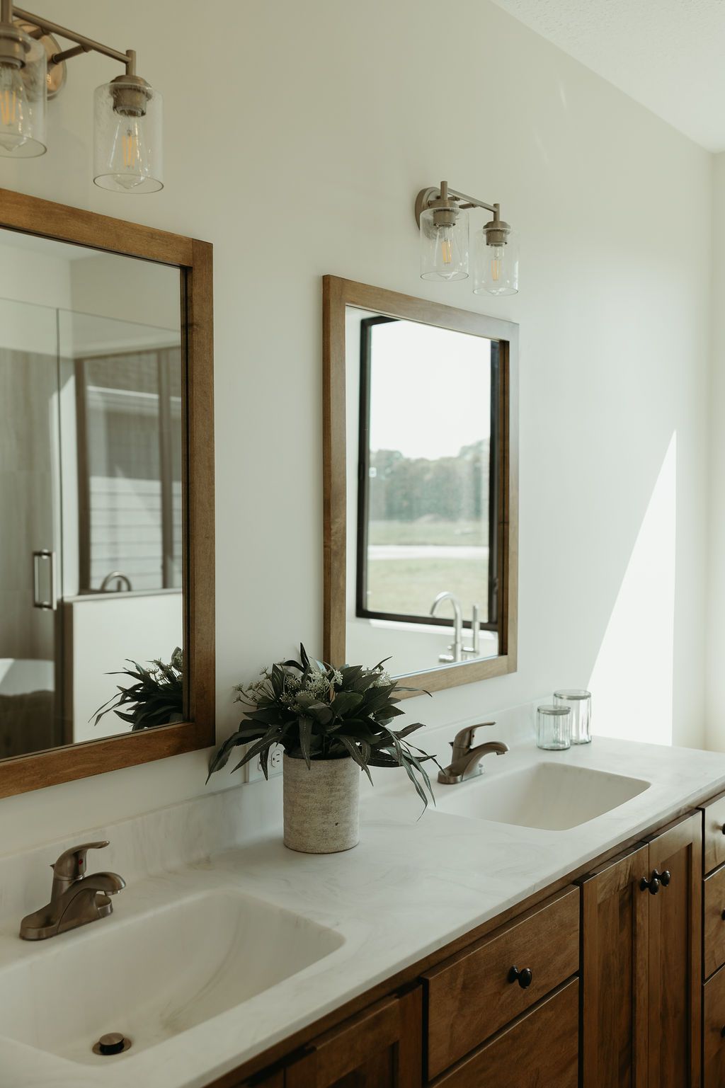 Bathroom with two sinks, wood-framed mirrors, and a floral arrangement on a white countertop.