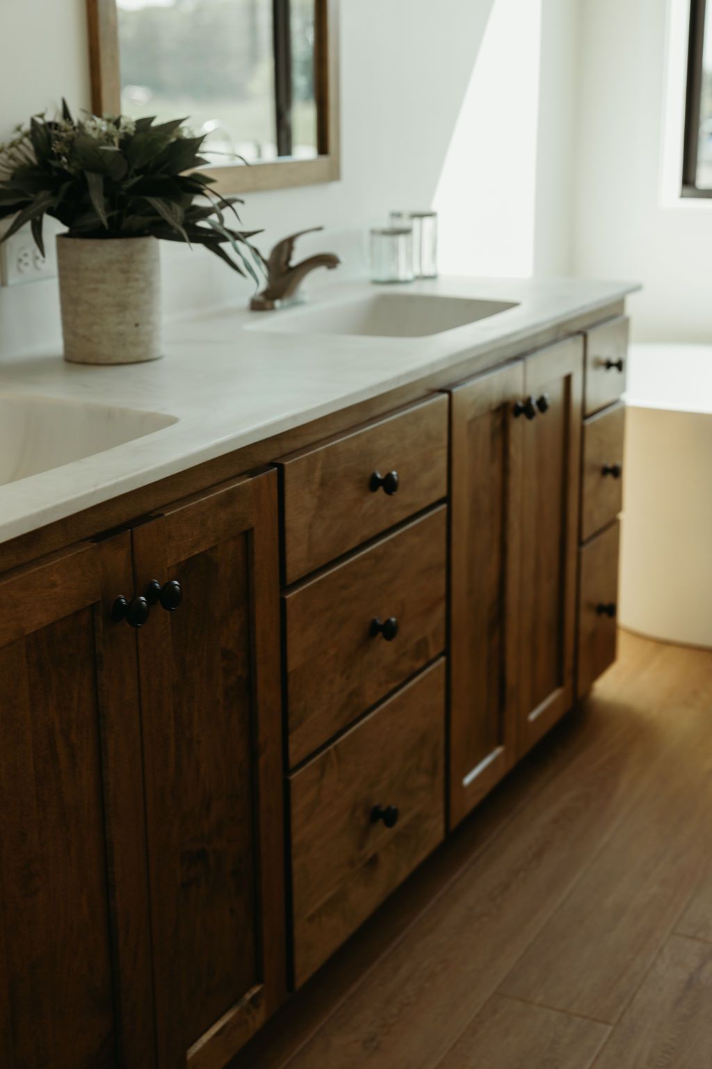 Wooden bathroom vanity with two sinks, dark hardware, and a plant.