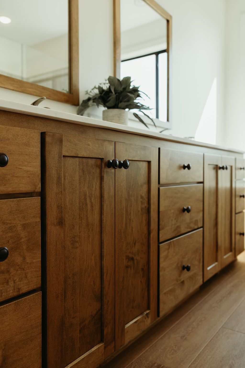 Wooden bathroom vanity with black hardware, white countertop, and mirror.