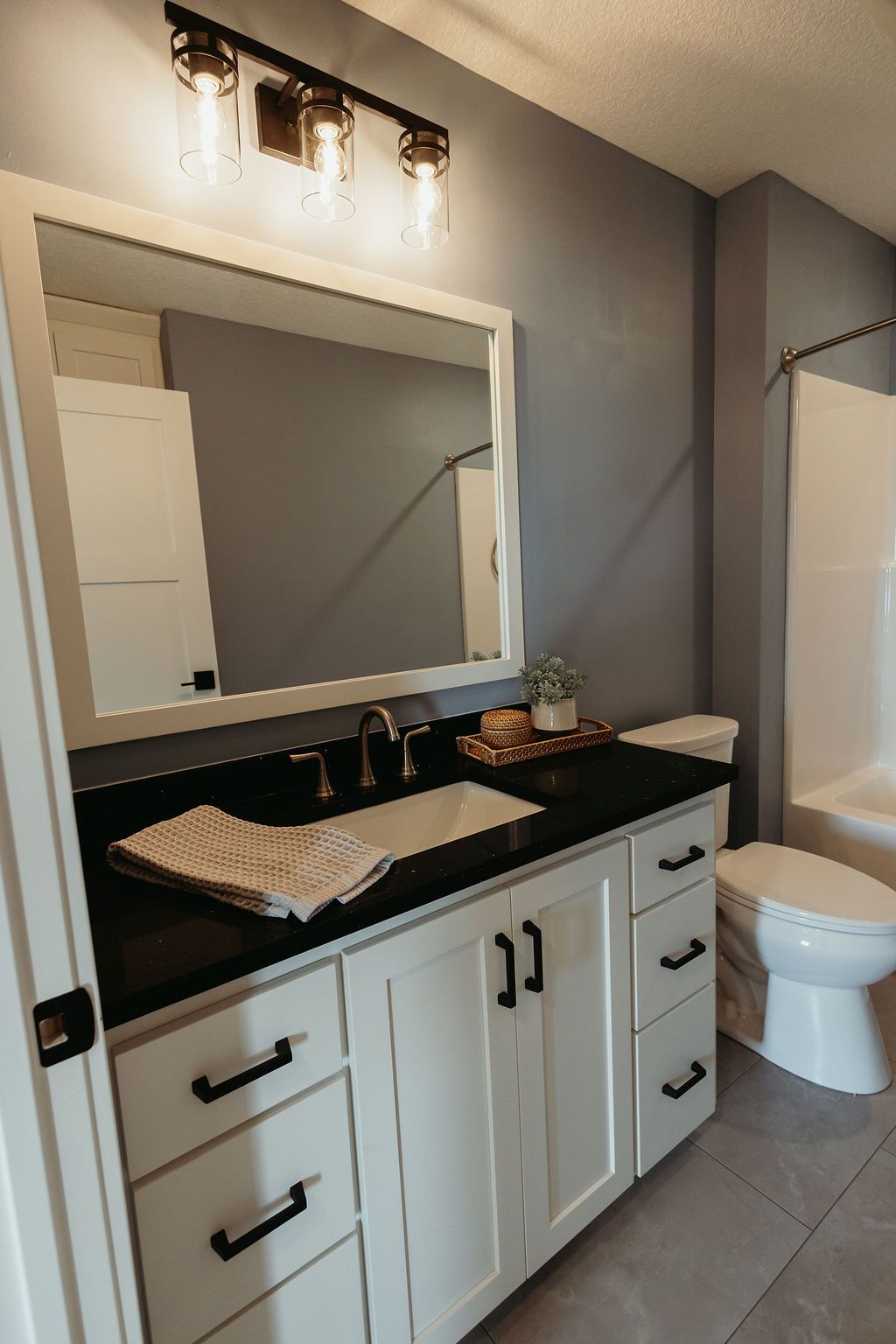 Bathroom with white vanity, black countertop, large mirror, and gray walls.