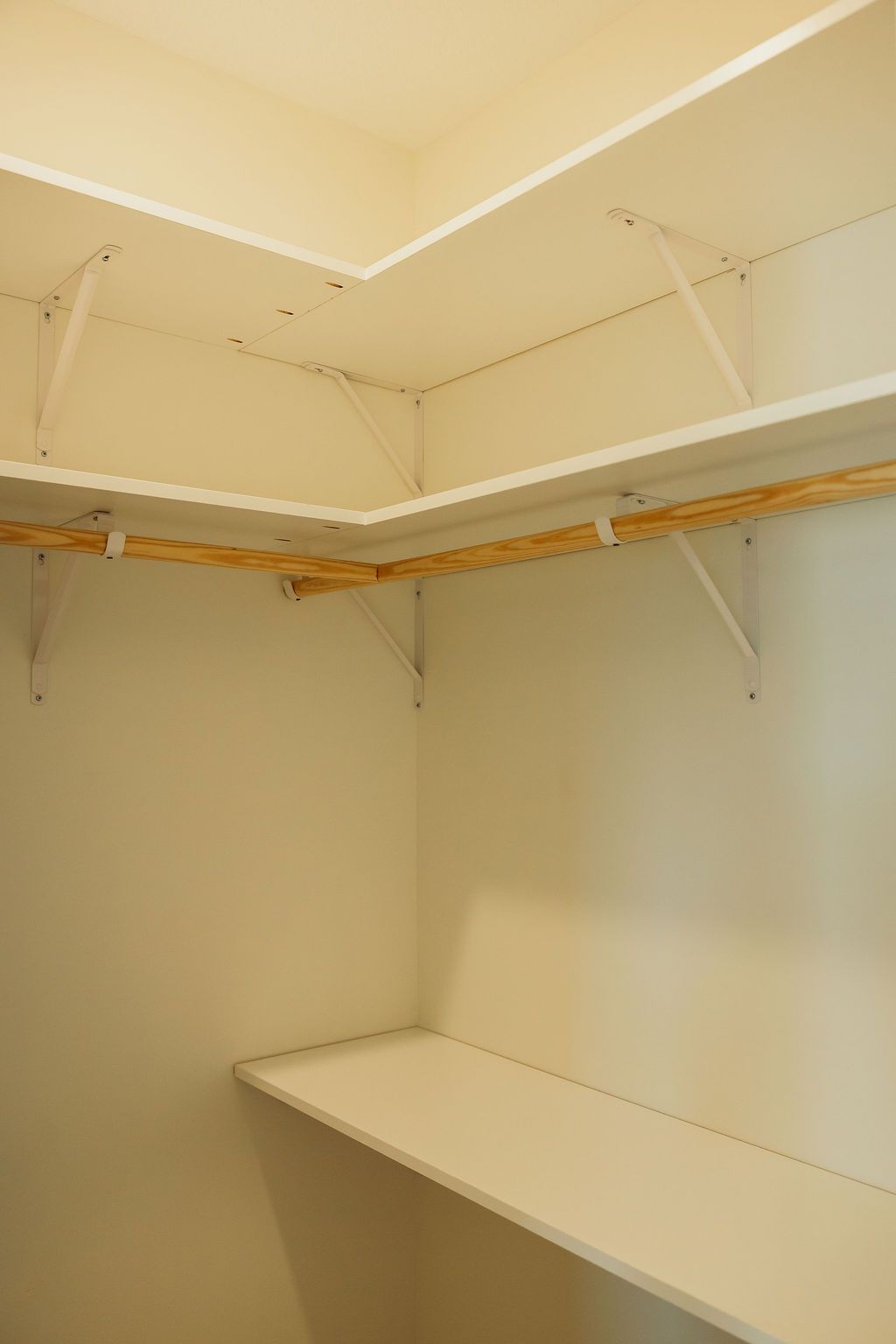Empty walk-in closet with white shelves, angled corner, and wooden hanging rod.