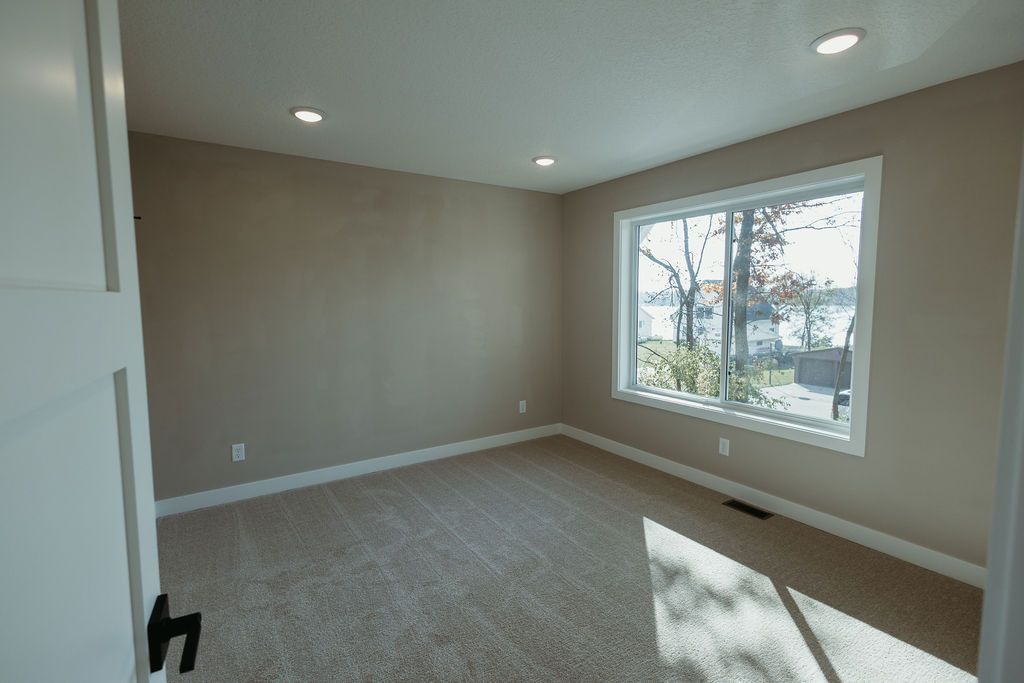 Empty room with tan walls, carpet, and a window overlooking trees.