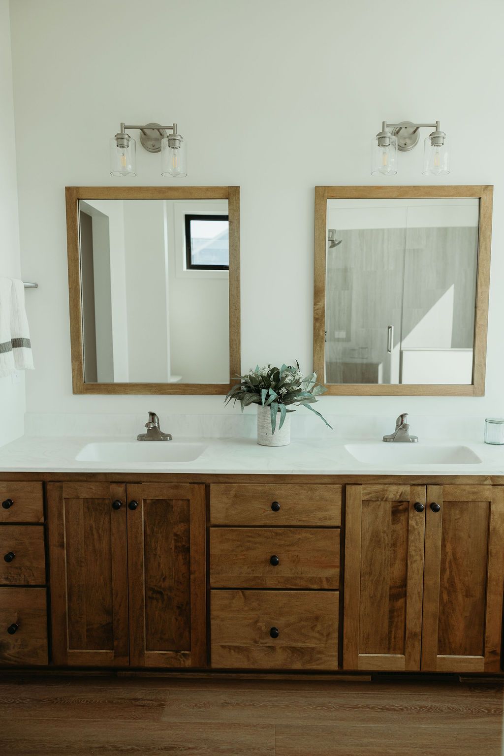 Bathroom with wood vanity, two mirrors, white countertop, and silver fixtures.