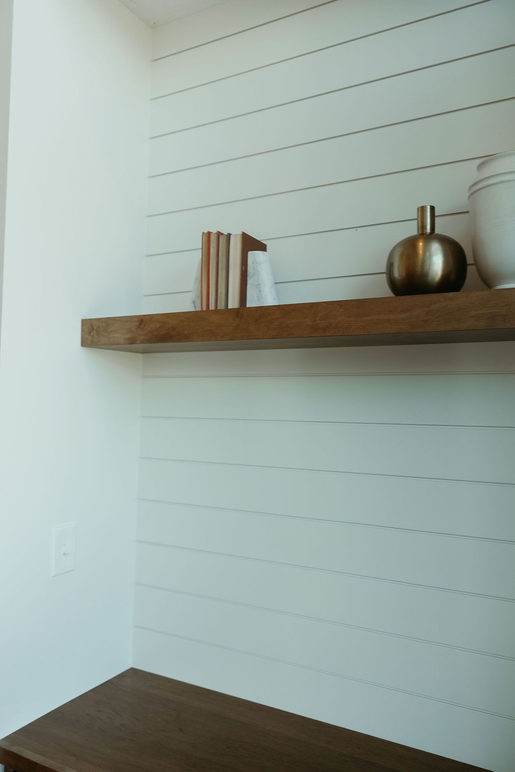 Wooden shelves with decor on shiplap wall; includes books and a gold vase.