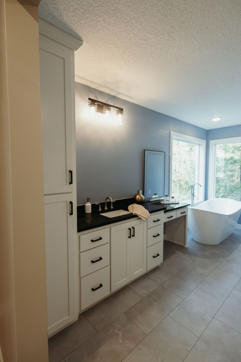 Bathroom with white cabinetry, black countertops, blue walls, and a white soaking tub.