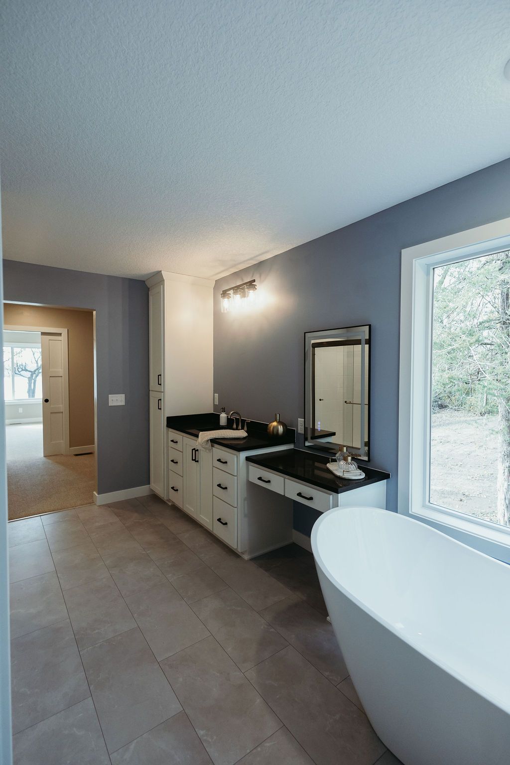 Bathroom with a white freestanding tub, vanity, and window with outdoor view. Light gray walls.