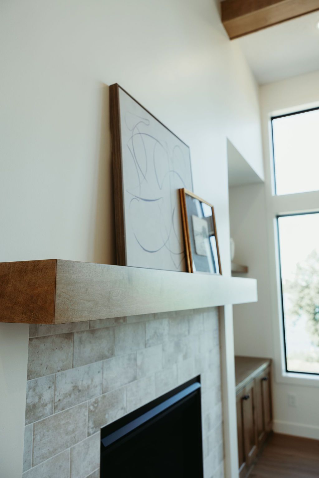 Fireplace with textured tile, light-colored mantel, and artwork, next to a tall window.