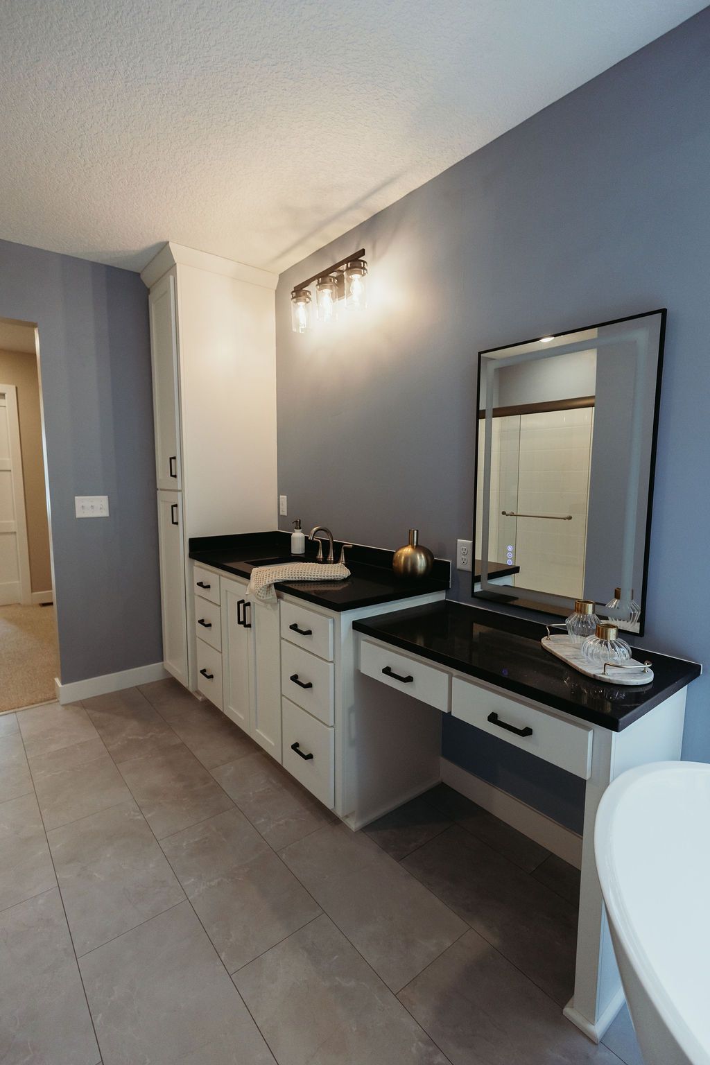 Bathroom with a white vanity, black countertop, and large mirror. Blue walls and light wood floor.