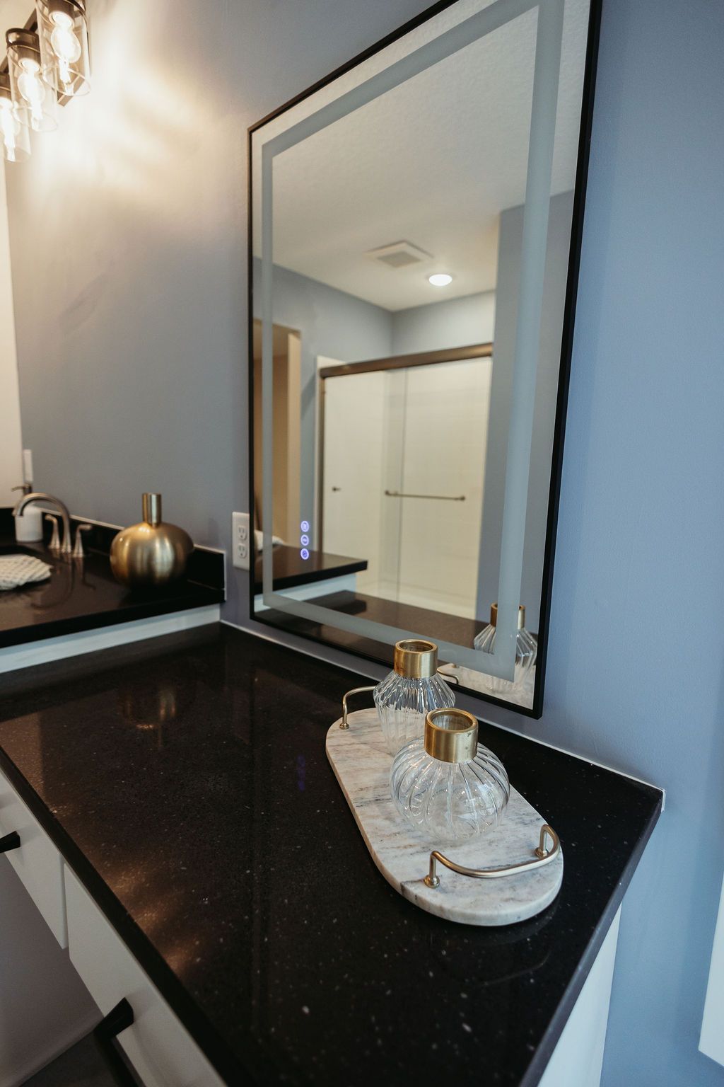 Bathroom with black countertop, gold accents, large mirror reflecting a shower.