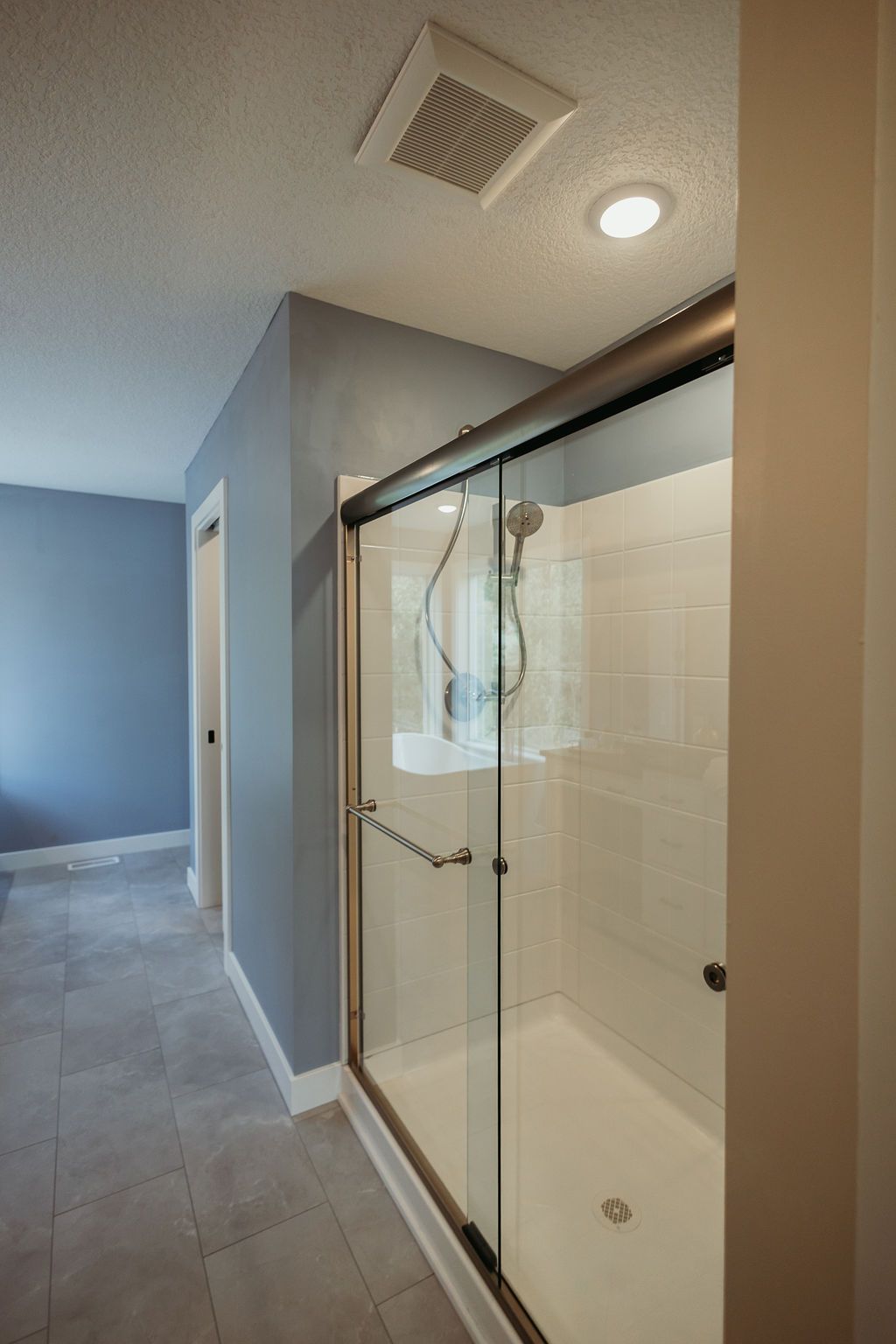 Modern bathroom with glass shower door, light gray walls, and tile flooring.