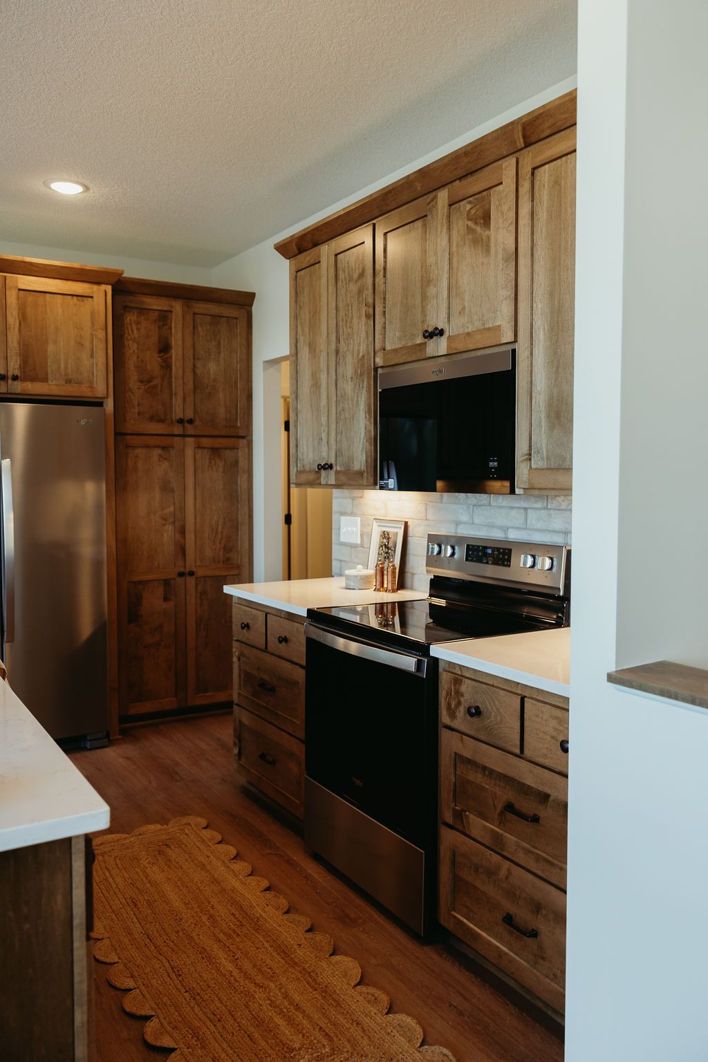 Kitchen with light wood cabinets, stainless steel appliances, and a woven rug.