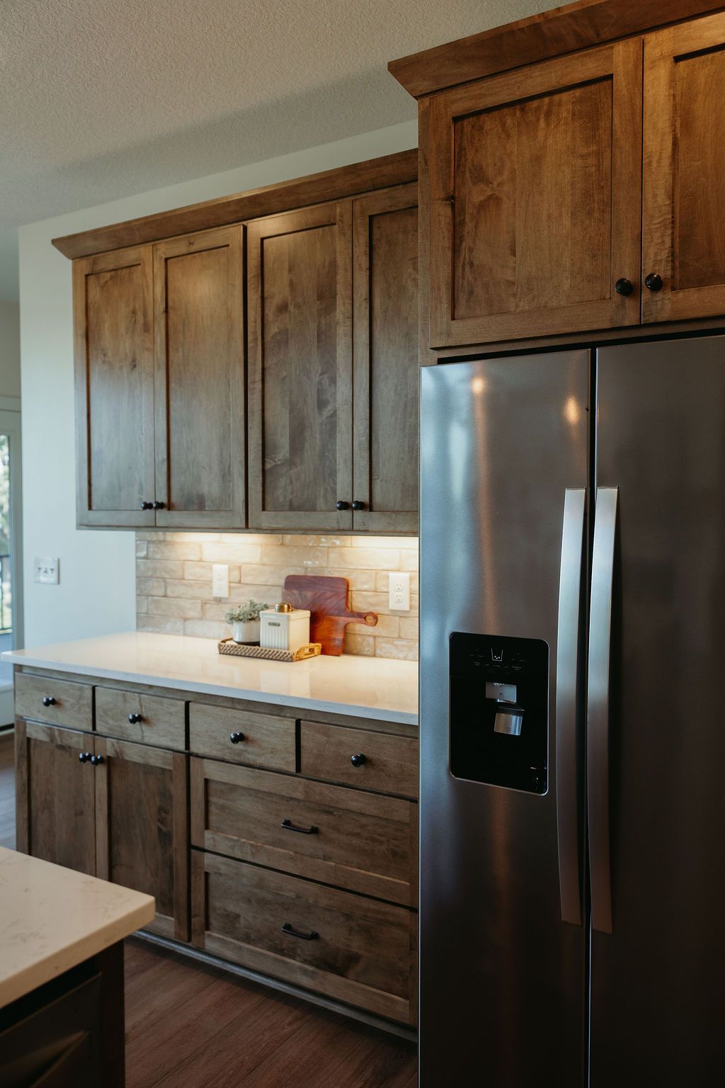 Wooden kitchen cabinets with stainless steel refrigerator and light-colored countertops.