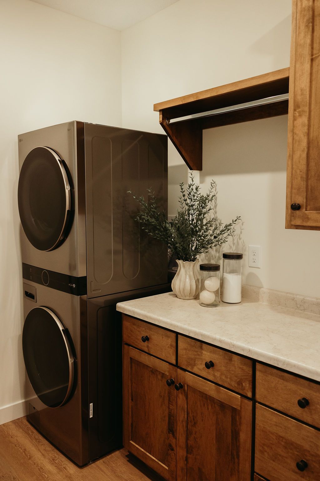 Stacked washing machine and dryer, wooden cabinets, countertop, and a small shelf in a laundry room.