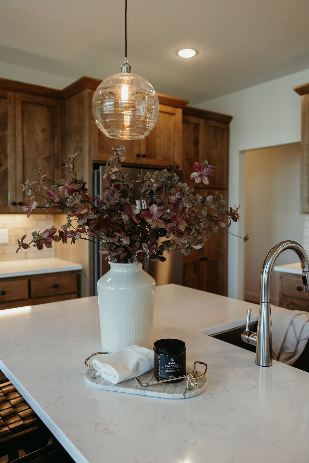 Kitchen island with floral arrangement, pendant light, and tray with candle and cloth, set against wood cabinets.
