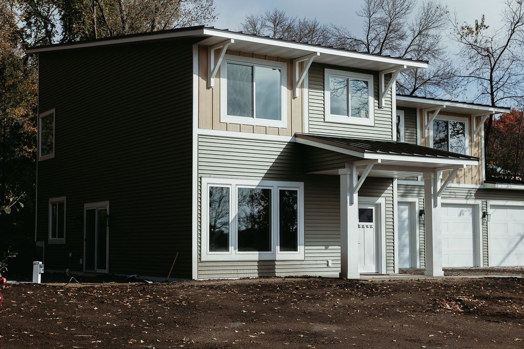 Two-story house with light and dark siding, white trim, and a small porch.