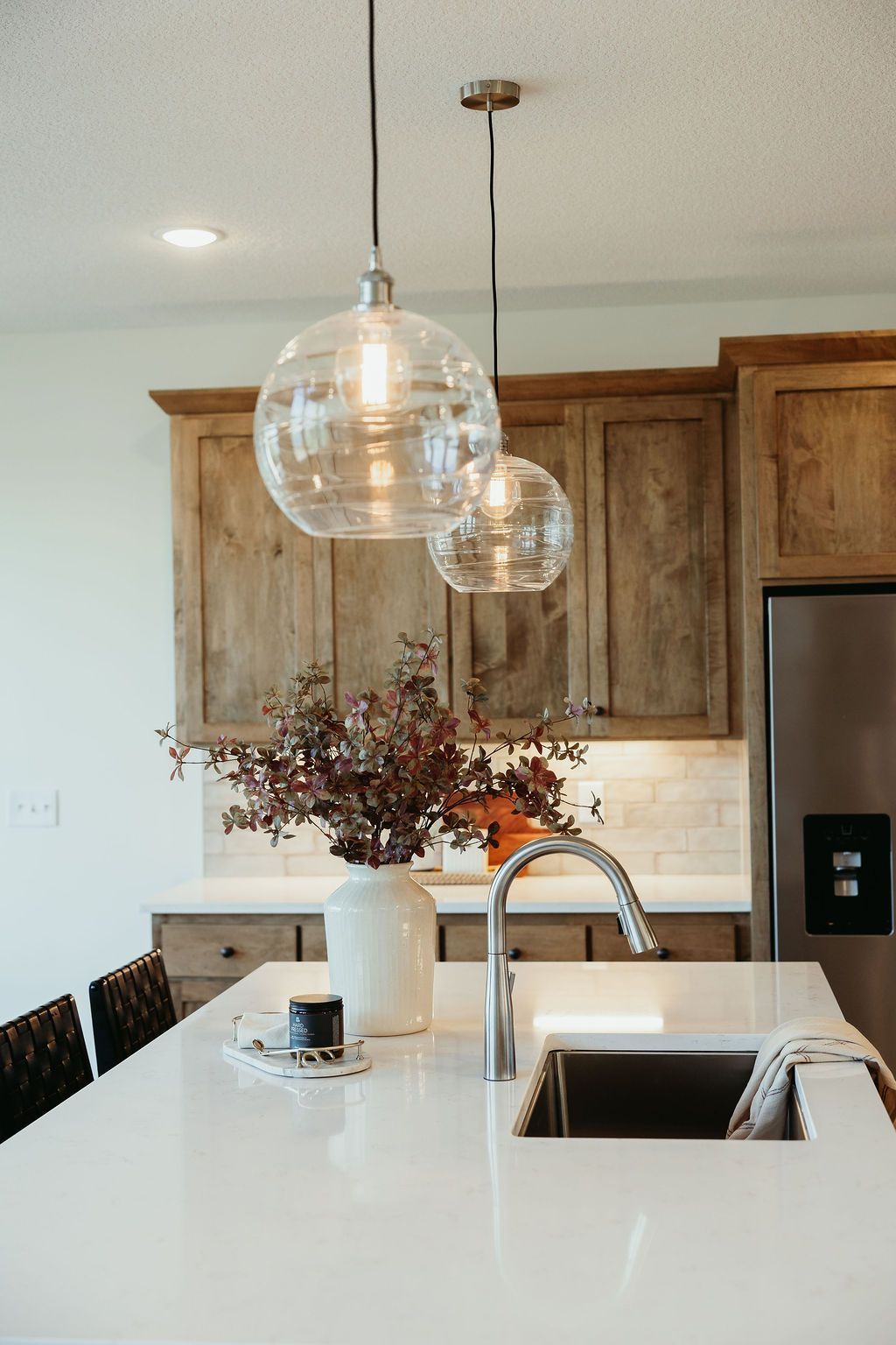 Kitchen island with clear globe pendant lights, white countertop, wooden cabinets, and a stainless steel faucet.