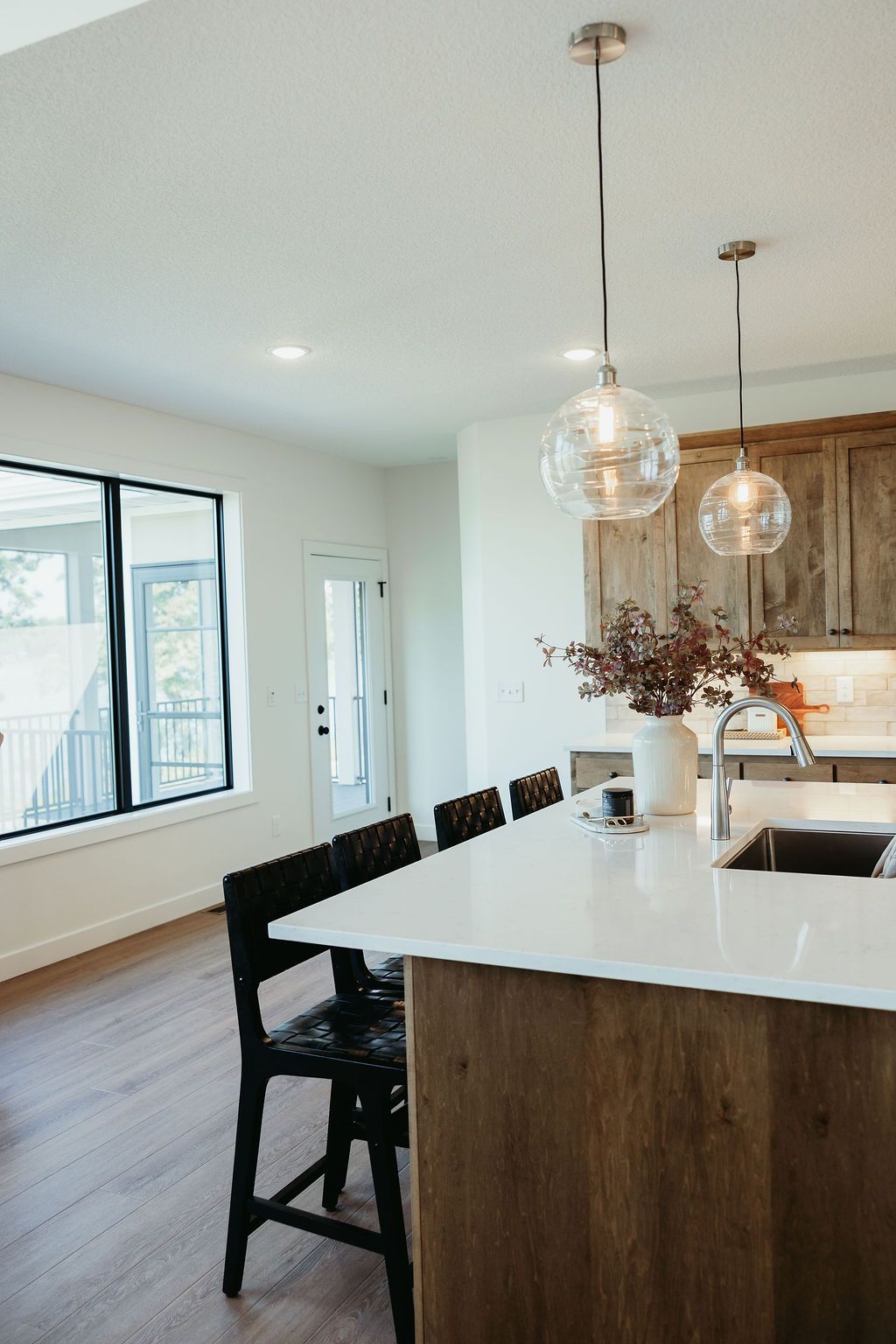 Kitchen with white countertop, wooden island, black chairs, and globe pendant lights.