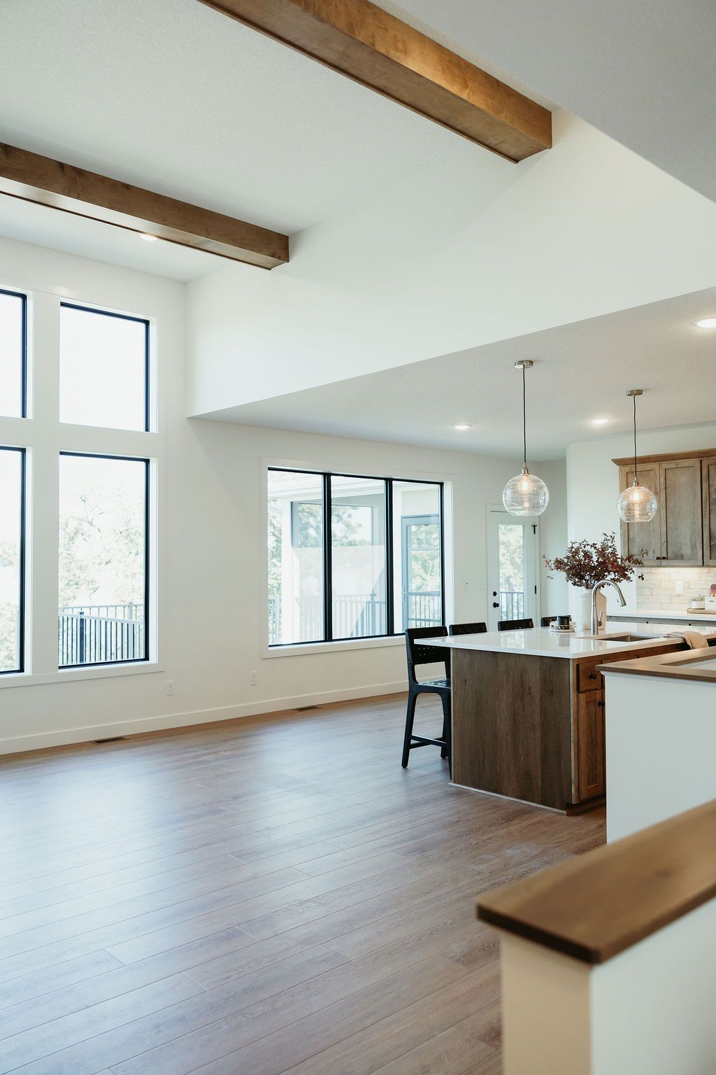 Open-concept kitchen and living room with wood flooring, large windows, and exposed wooden beams.