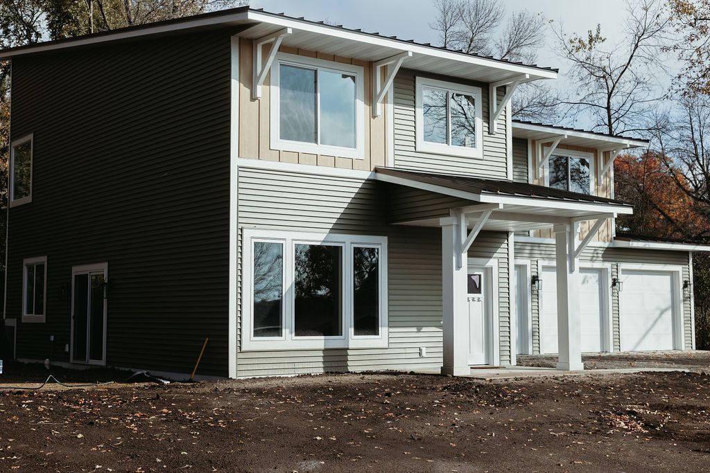 Two-story house with light green siding and white trim. Features include large windows and a front porch.