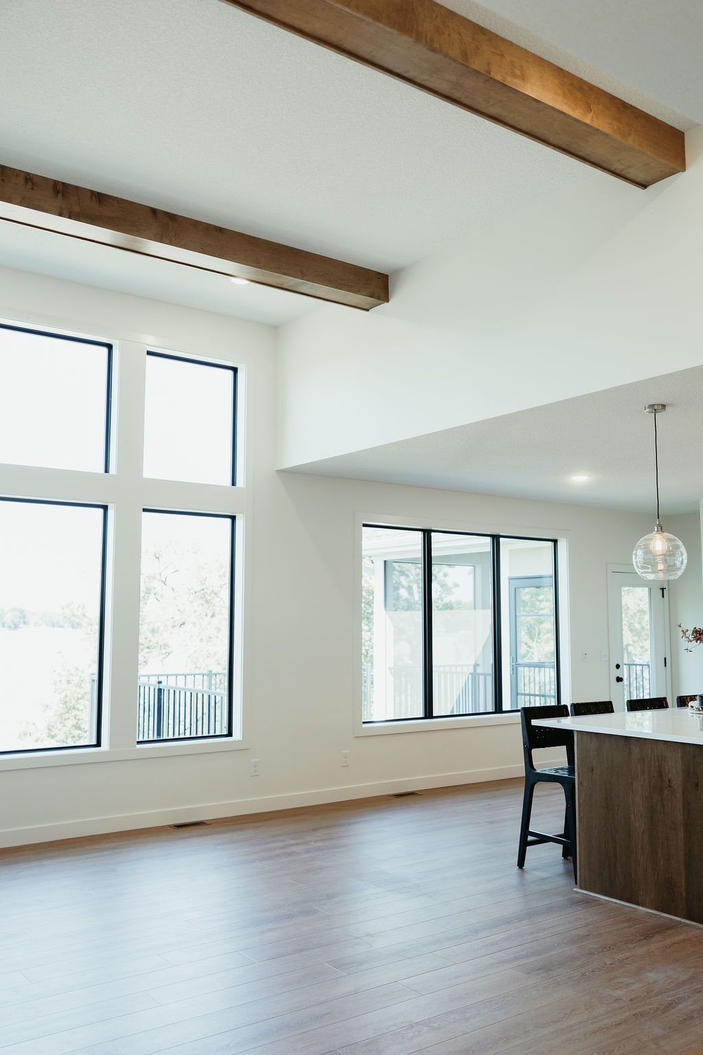 Modern living room with high ceilings, large windows, wood beams, and hardwood floor.
