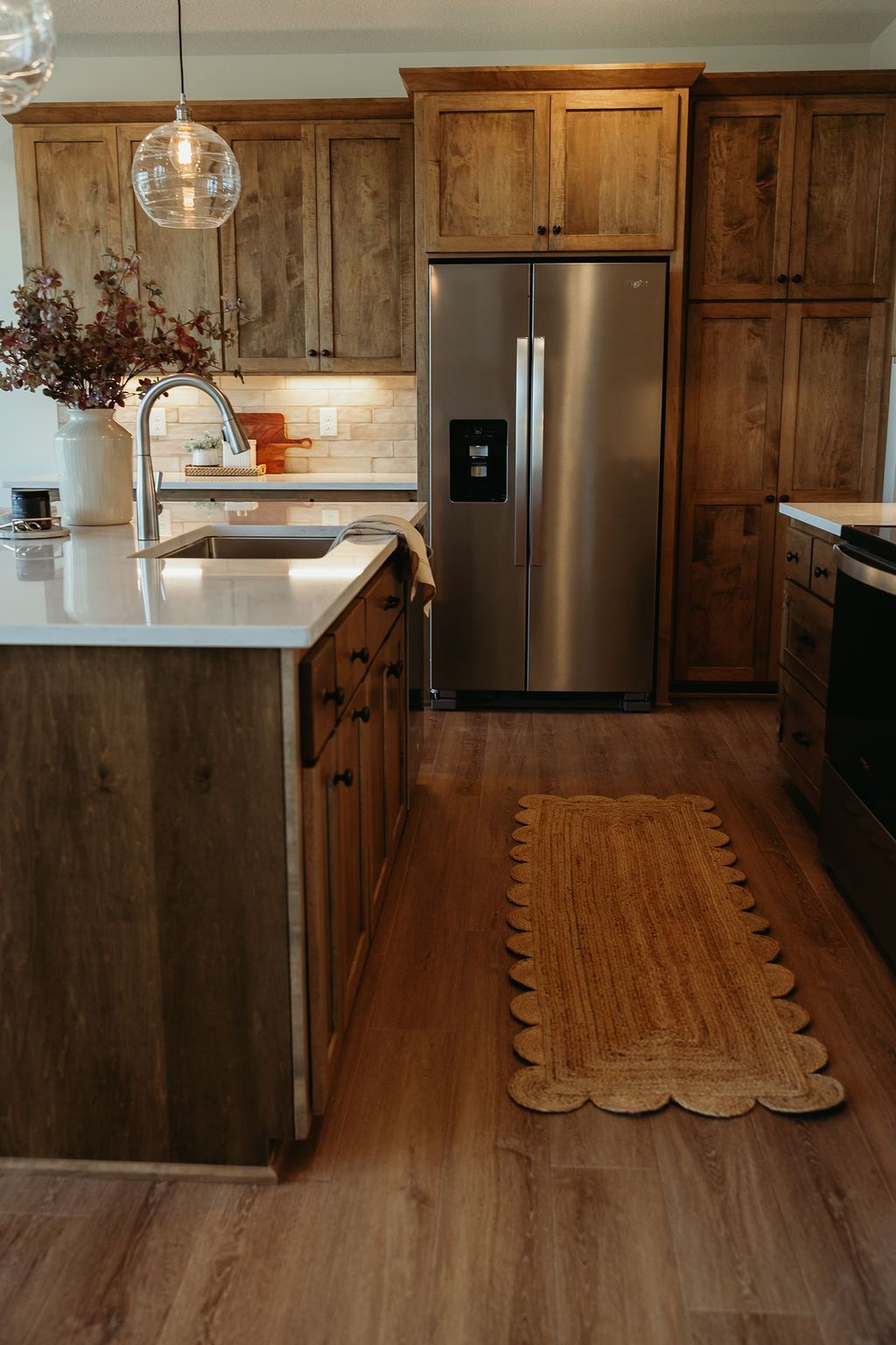 Kitchen with wood cabinets, stainless steel refrigerator, and a rug on wood-look flooring.