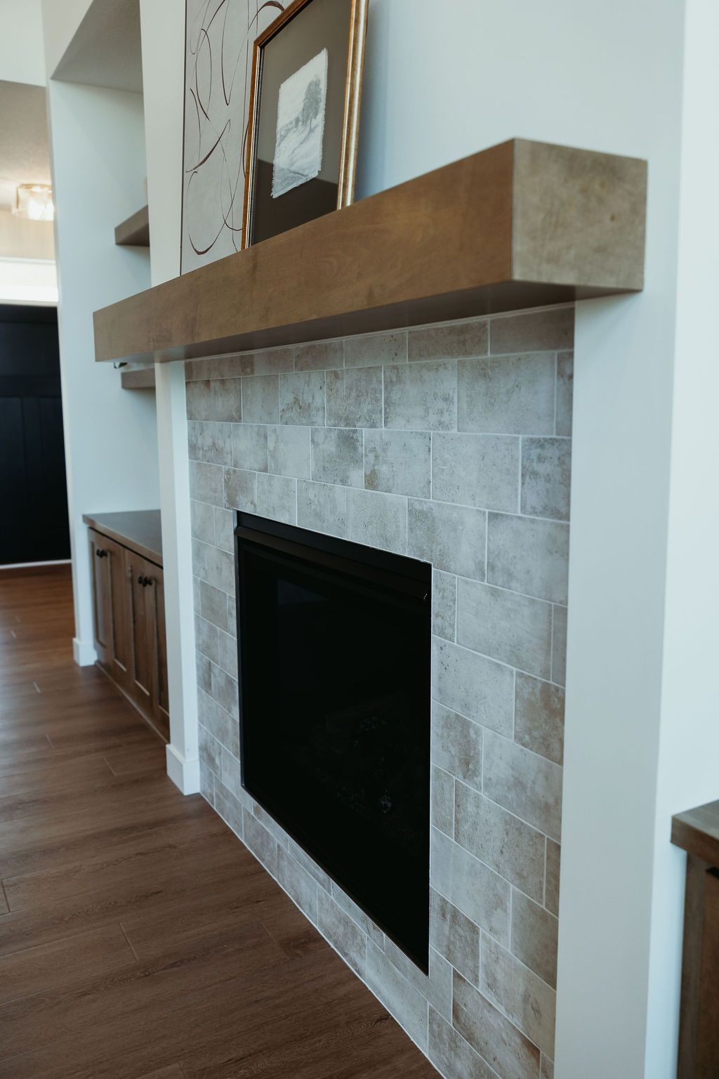 Fireplace with light grey brick tile, a dark wooden mantel, and a black fireplace insert.