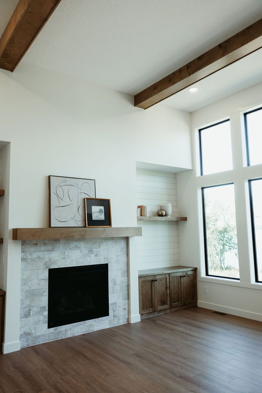 Living room with fireplace, white walls, wooden beams, and large windows.