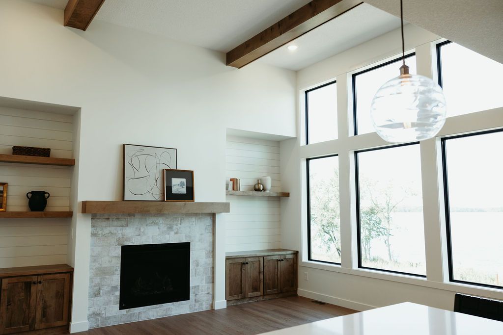 Living room with fireplace, large windows, wood beams, and a pendant light.