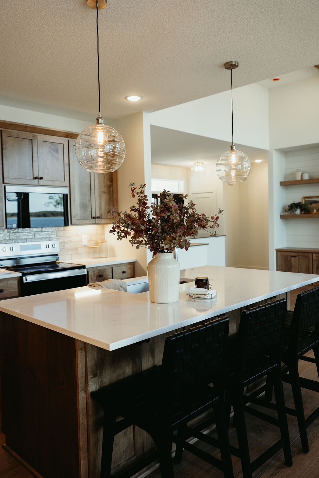 Modern kitchen with island, pendant lights, wooden cabinets, and bar stools.