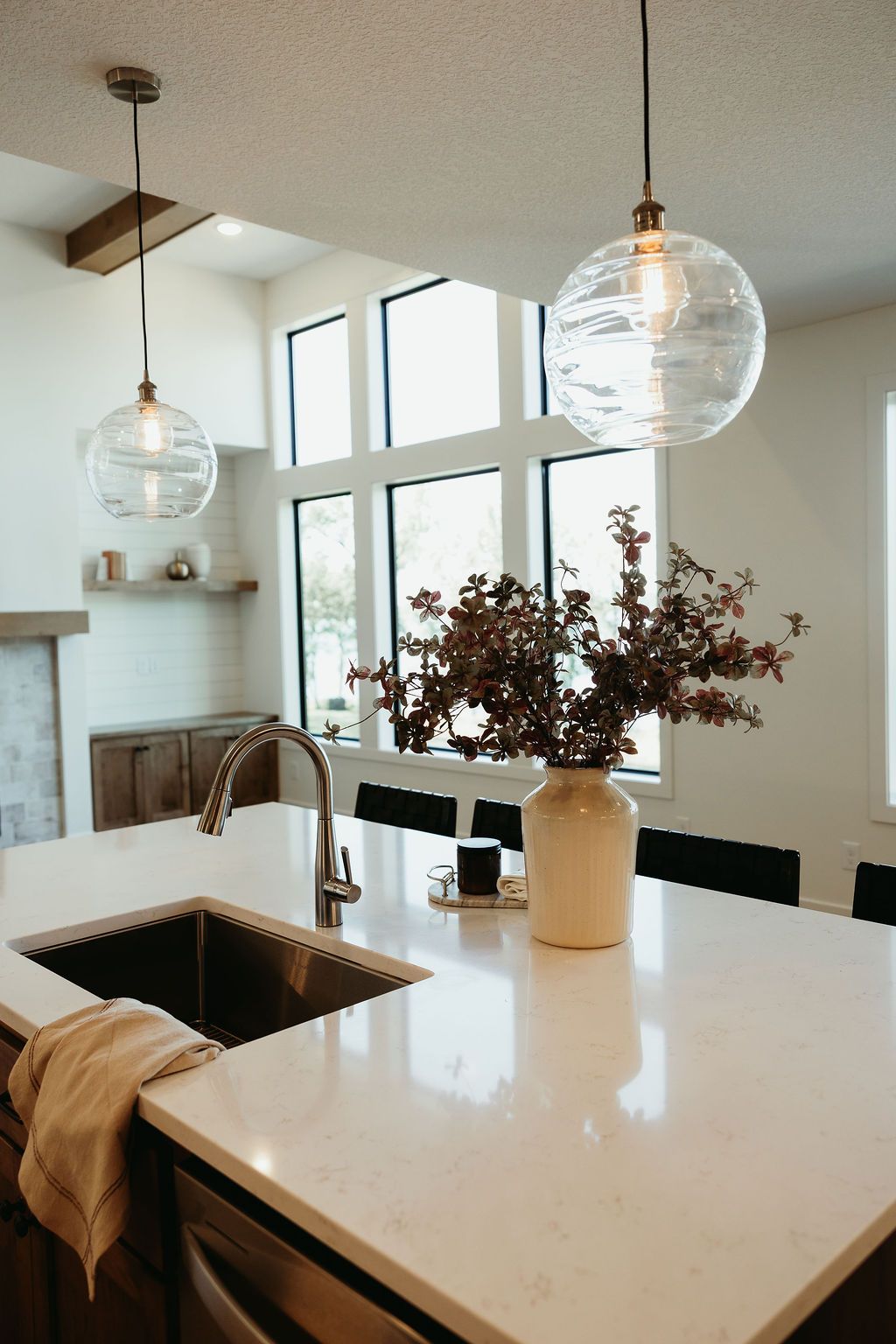 Modern kitchen with island, pendant lights, large windows, and floral arrangement.