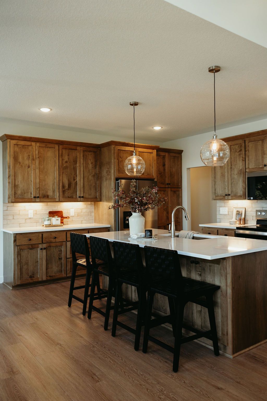 Kitchen with wooden cabinets, white countertops, black bar stools, and pendant lights.