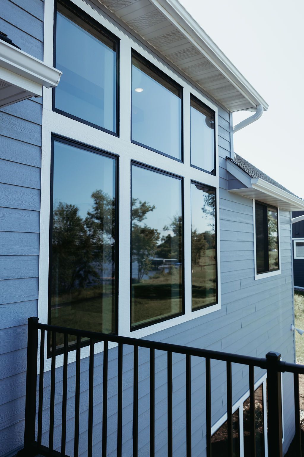 Blue house with large grid windows reflecting the outside, black railing below.