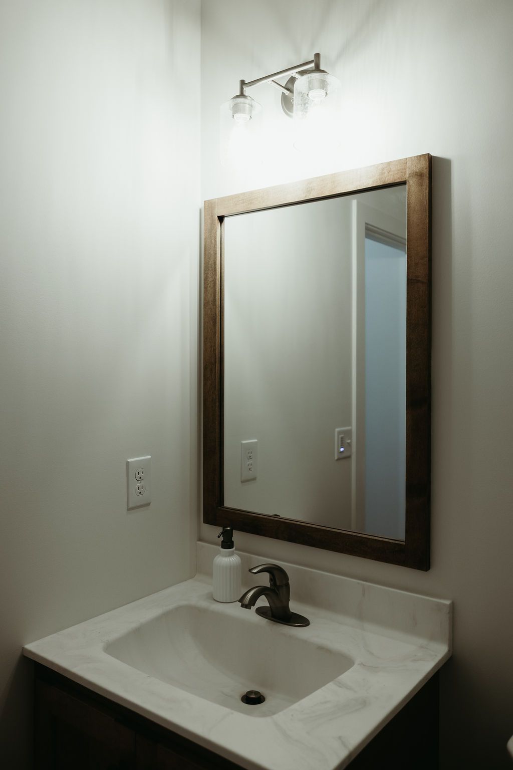 Bathroom with a white sink, marble countertop, and a framed mirror. A light fixture is above the mirror.