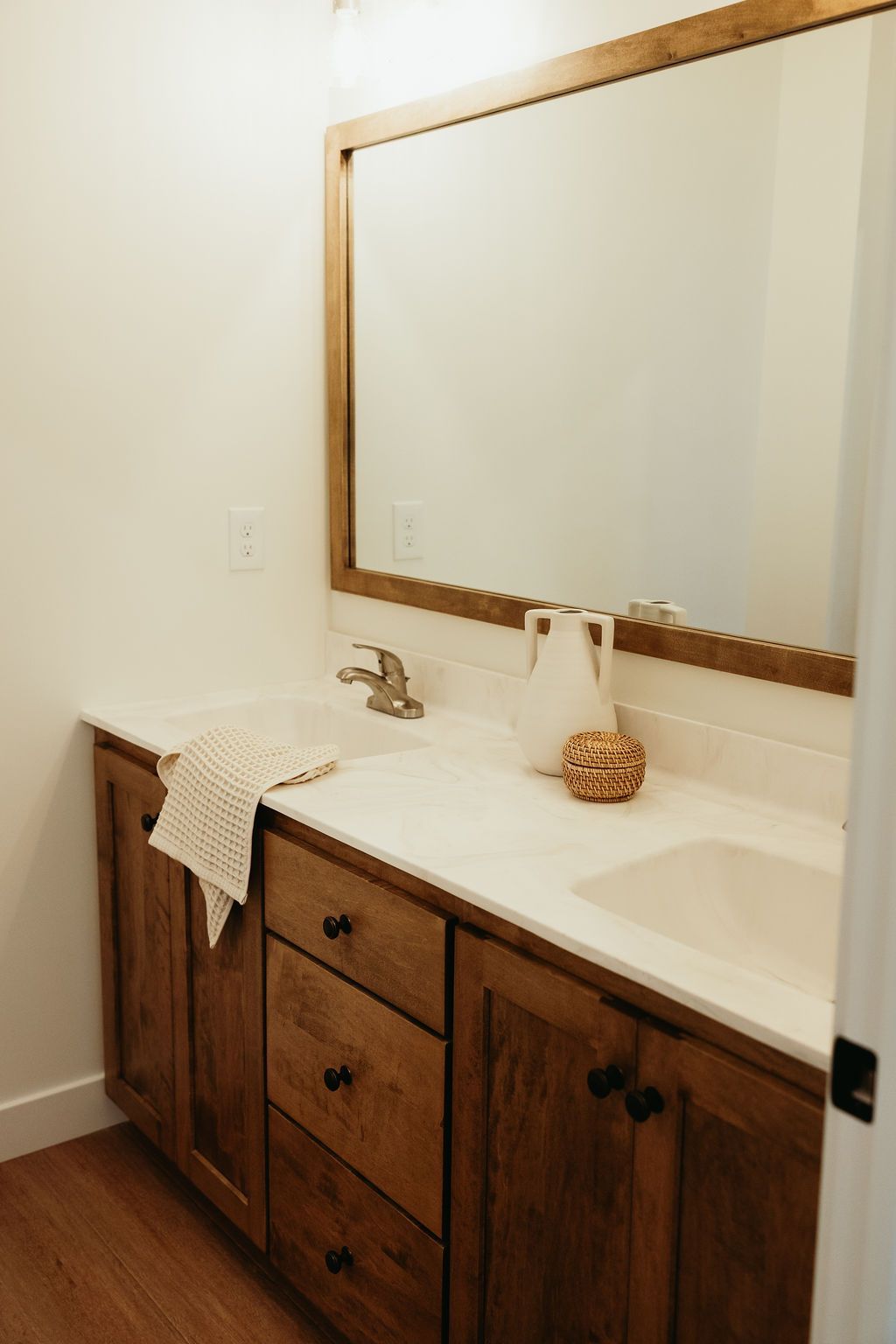 Bathroom vanity with wooden cabinets, white countertop, large mirror, and decorative items.