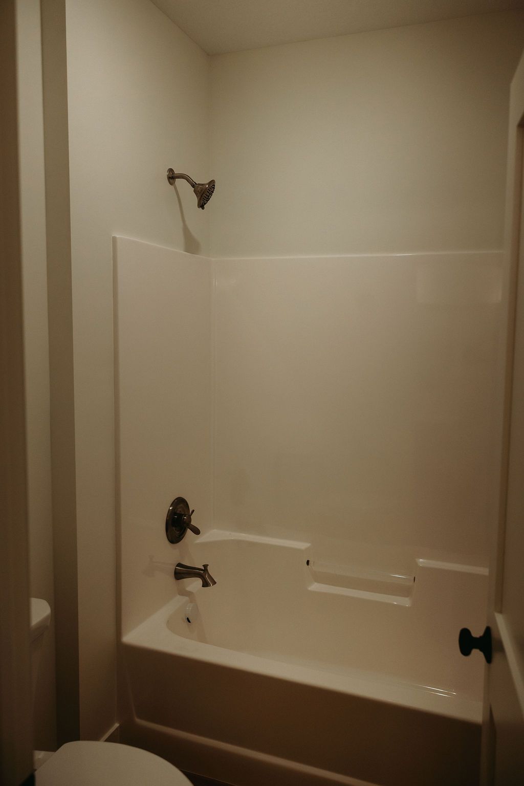 A small, white bathroom with a shower/tub combo; silver showerhead and faucet.