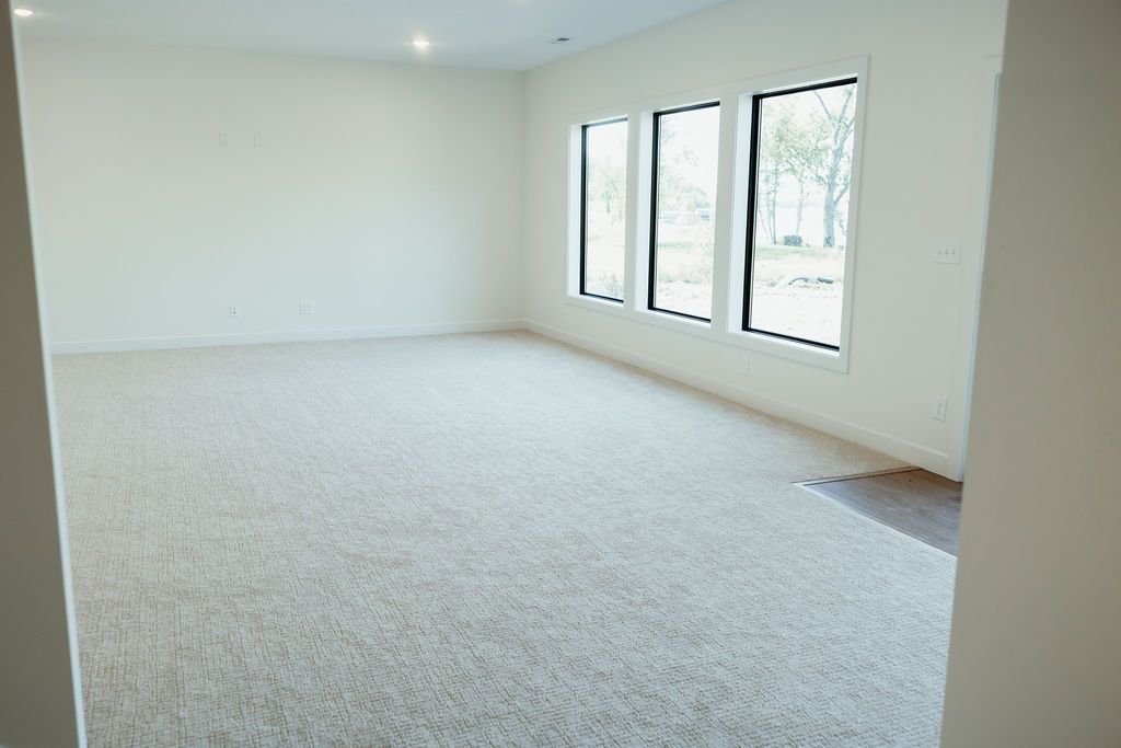 Empty room with white walls, carpet, and three windows.