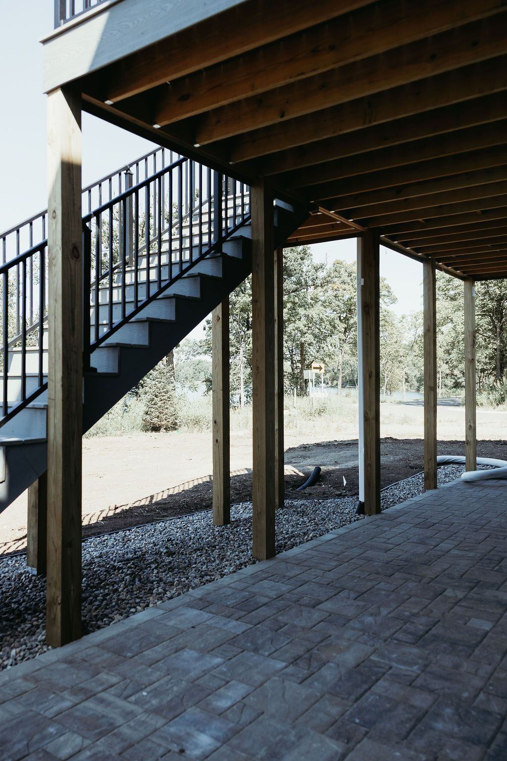 Wooden deck with black railing and stairs leading down to a brick patio supported by wooden posts.