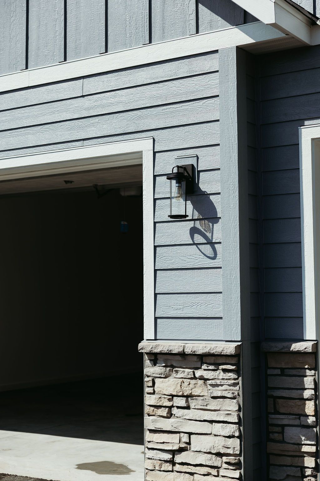 Exterior of a house with a garage, blue siding, stone columns, and a black light fixture.
