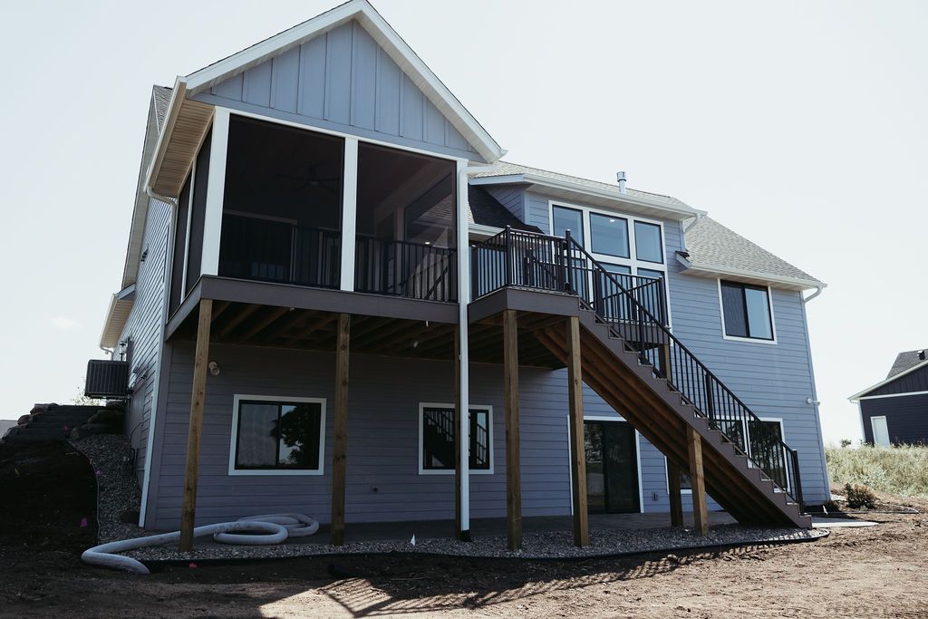 Two-story house with a wooden deck and staircase. Exterior is blue siding, a screened porch.