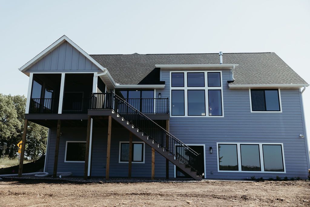 Blue two-story house with a screened porch, dark stairs, and large windows against a clear sky.