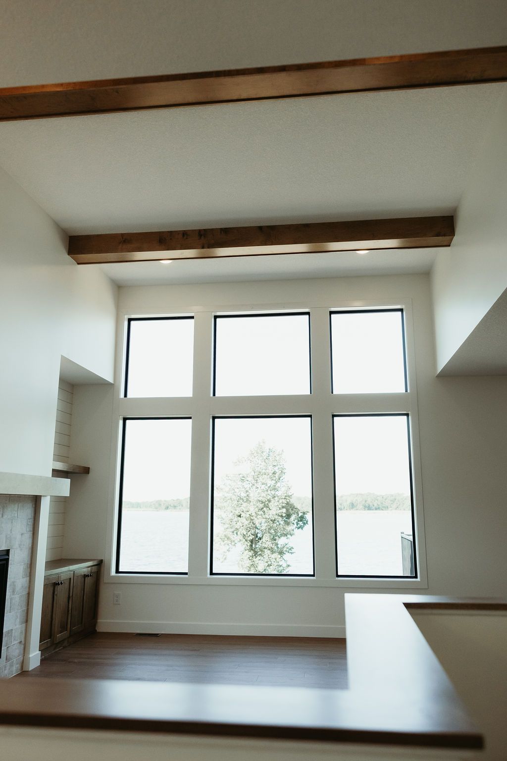 Large windows overlooking water, wooden beams, fireplace in a bright, modern interior.