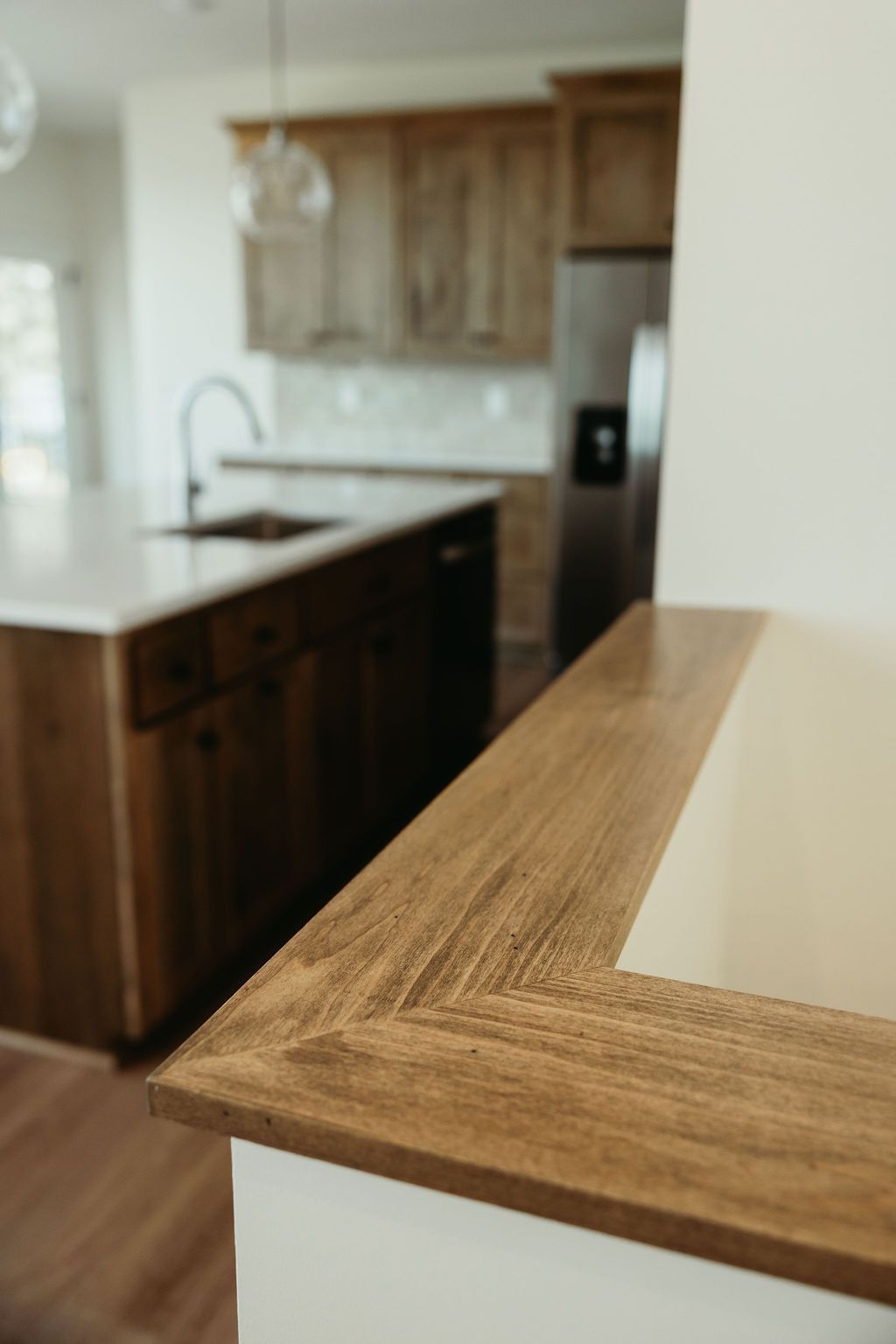 Wooden countertop detail in a modern kitchen with a white wall and island in the background.