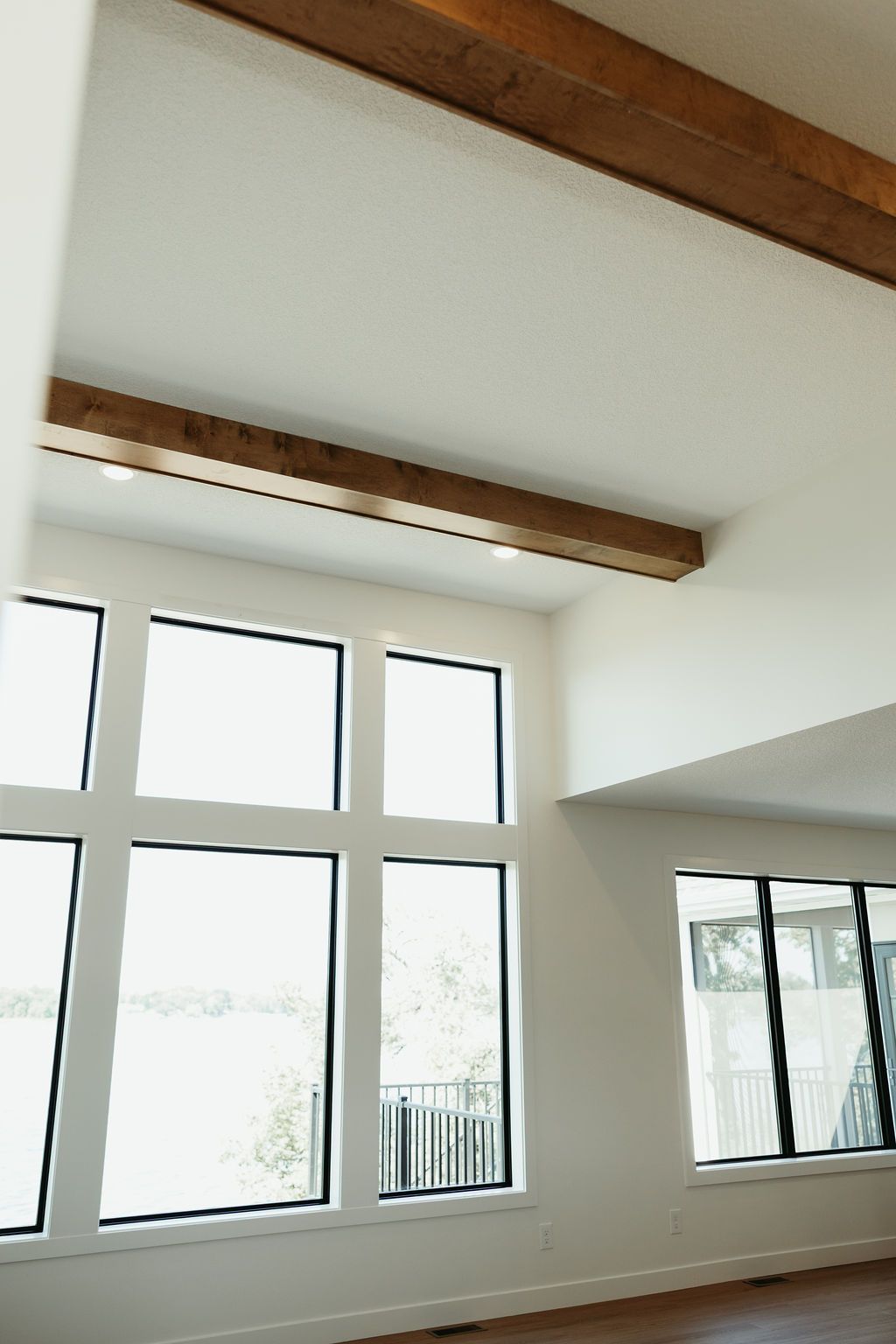 Interior view of a room with large windows, white walls, and wooden beams on the ceiling.