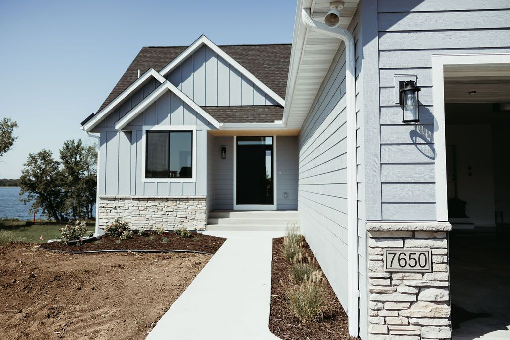 Light blue house with stone accents, concrete path, and open garage on a sunny day.