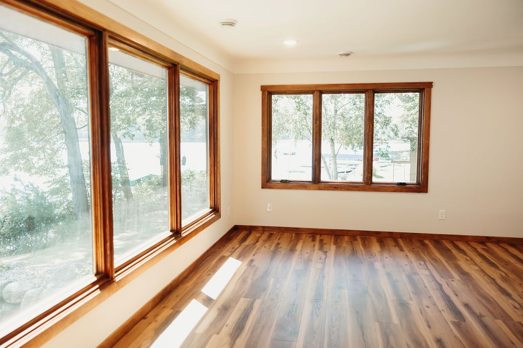 Empty room with large wooden-framed windows overlooking a green landscape. Wooden floor, cream walls.