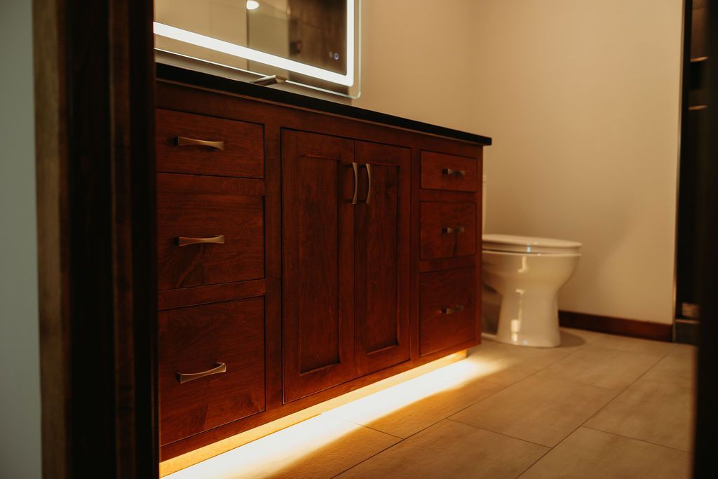 Bathroom vanity with under-cabinet lighting, dark wood cabinets, and a toilet.