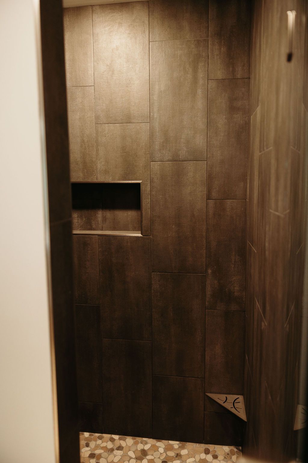 Dark tiled shower with built-in shelf and pebble floor.