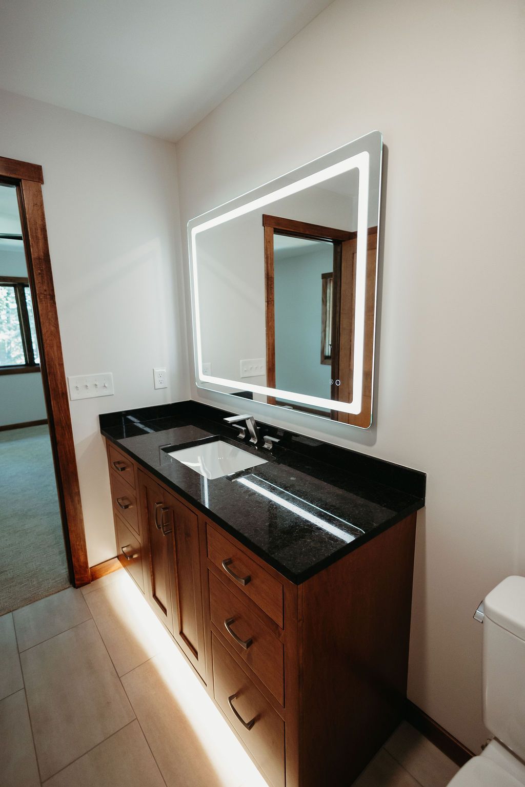 Bathroom vanity with a dark countertop and a large mirror with LED lighting.